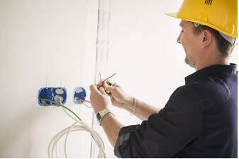 Electrician with yellow hard hat prepping red yellow blue wires for installation of electrical switches 