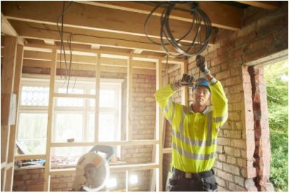 Electrical contractor with yellow vest and blue hard hat running wire inside residential home